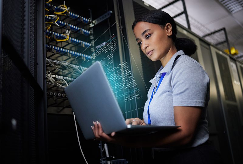 Woman working with laptop in server room.